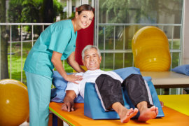 nurse assisting elderly man doing physical therapy